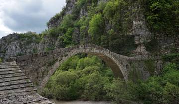 An ancient stone bridge over a lush green gorge.