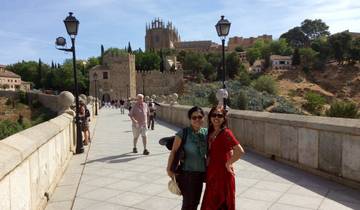 People standing on a stone bridge with a historic city in the background.