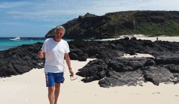 Man posing on a beach with rocky terrain in the background.