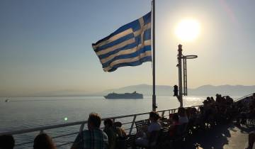 Greek flag waving on a ferry with passengers enjoying the sea view.