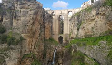 A historic stone bridge over a gorge with a waterfall below