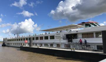 A large river cruise ship docked with blue sky and clouds.