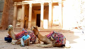 Two camels and a person in front of the Petra Treasury.