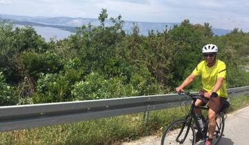 A man cycling along a road with a scenic view of the sea.