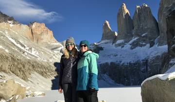 Two people posing in winter clothing in front of snowy mountains.