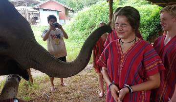 Person smiling as an elephant touches their shoulder with its trunk.