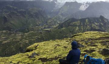 Hiker sitting on a mossy mountain with a vast valley view.