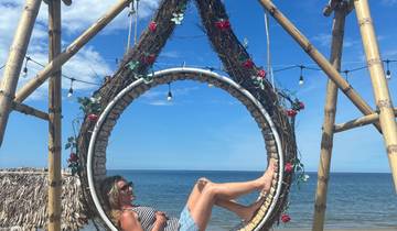 Woman posing inside a decorative circular swing structure by the beach.