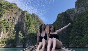 Two women sitting on a boat with cliffs in the background.