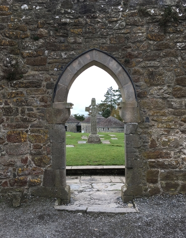 Stone arch framing a Celtic cross in a field.