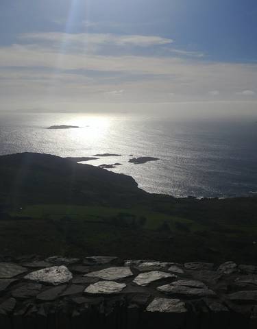Scenic view of the ocean with sunlight reflecting on the water and small islands in the distance.