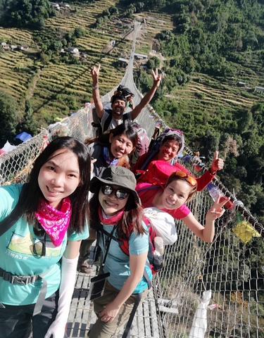 A group selfie taken on a suspension bridge with green landscapes around.
