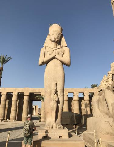 Ancient Egyptian statue standing tall against a blue sky.