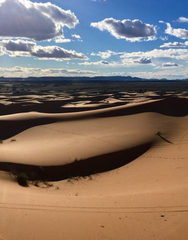 Expansive sand dunes under a bright sky with distant mountains.