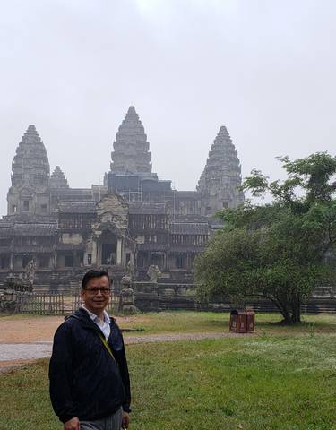A visitor at Angkor Wat surrounded by lush greenery.