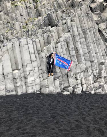 Person holding a flag standing on basalt columns.