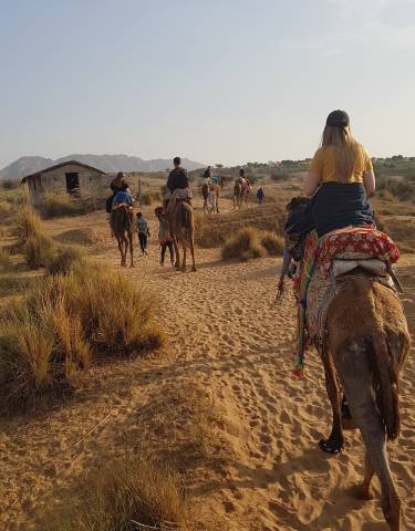 Group of people riding camels on a desert path.