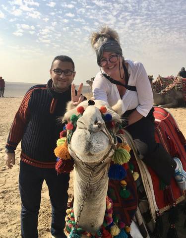 People posing on a camel beautifully decorated with colorful threads.