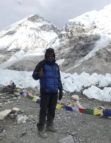 A man posing with a thumbs-up in a snowy mountainous area.