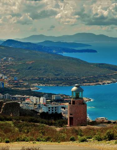 A coastal town with a lighthouse and sprawling mountain scenery.