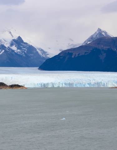 Snow-capped mountains and a glacier reaching a lake.