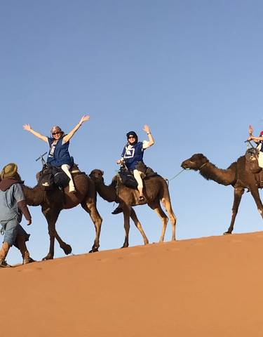 People riding camels on sand dunes with a guide.