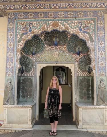 Woman standing in front of an intricately decorated archway with peacocks.