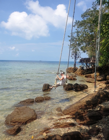 Person swinging on a rope over clear, calm sea.
