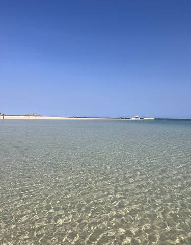 Shallow clear turquoise water with boats in the distance.