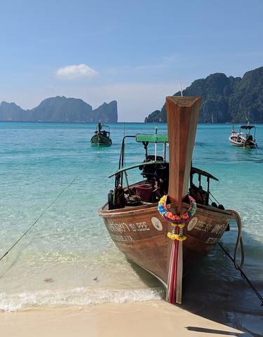 Traditional longtail boat anchored on a clear blue sea with distant islands.
