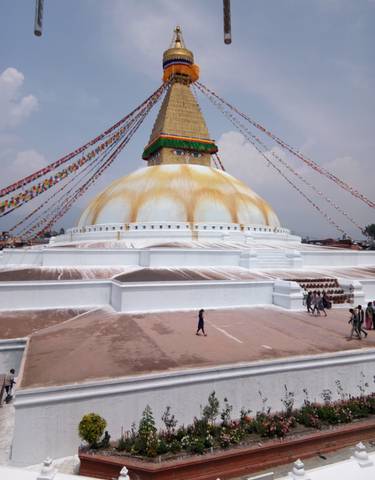 Large stupa with prayer flags and people walking around.