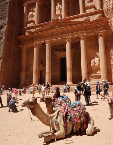 Visitors and camels in front of a grand, ancient rock-carved facade.