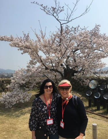 Two women posing in front of cherry blossoms.