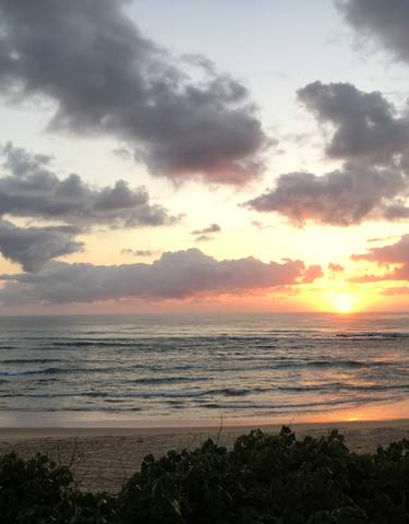 Beach at sunrise with waves lapping at the shore and clouds above.