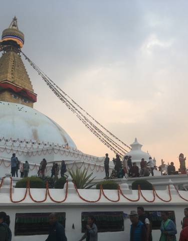 A large stupa surrounded by people, during sunset.