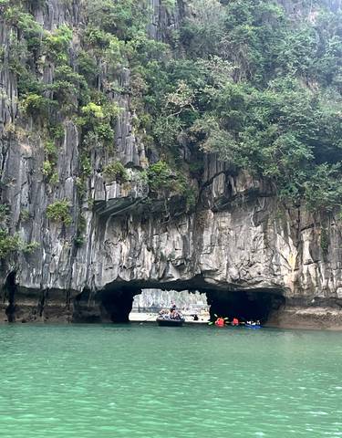 Boat entering a cave in a scenic limestone karst landscape.