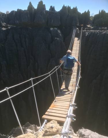 Person crossing a rope bridge over rock formations.