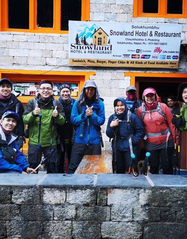 Group of hikers with trekking poles posing outside a restaurant.