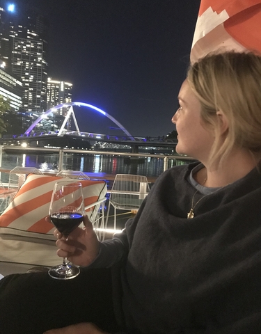 Person enjoying wine with a view of a lit-up bridge at night.
