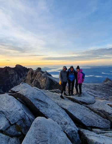 Three people posing on a rocky mountain peak at sunrise.