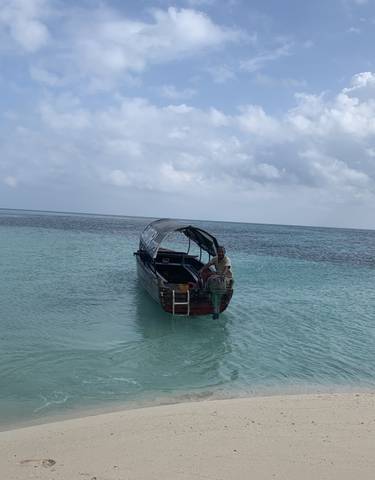 Boat on clear blue ocean water near a sandy beach.