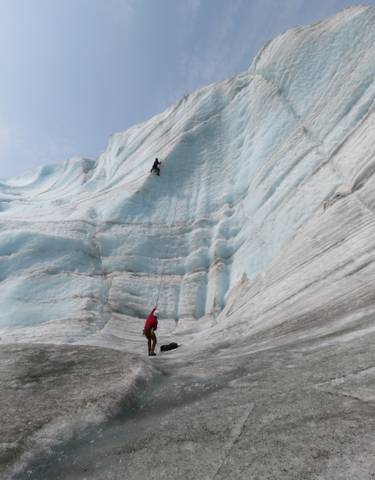 Two people climbing a large glacier.