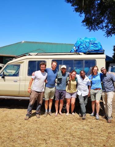 Group of people posing in front of a safari vehicle.