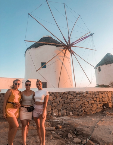 Three women posing in front of iconic windmills.