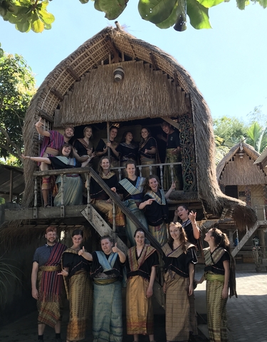 Group of people in traditional clothing posed on a wooden structure.