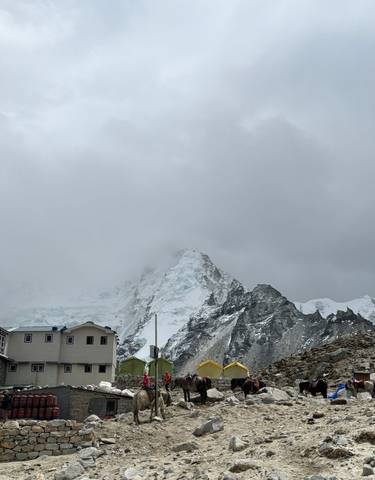 Camp at the base of a snowy mountain with clouds overhead.