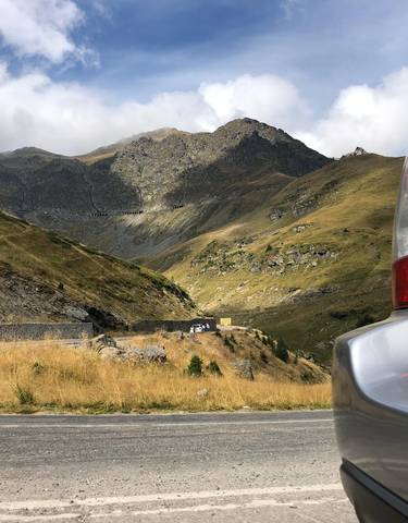 A scenic mountain road with a car parked to the side.