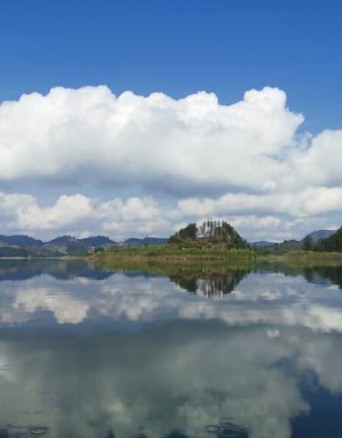 A reflective lake with clouds and lush surroundings.