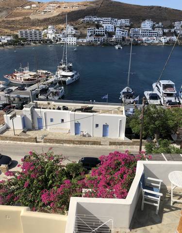 White buildings with blue doors near a dock with boats and a Greek flag.