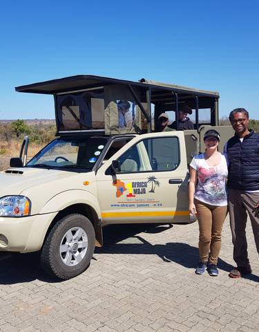 Couple posing in front of a safari vehicle in a dry landscape.
